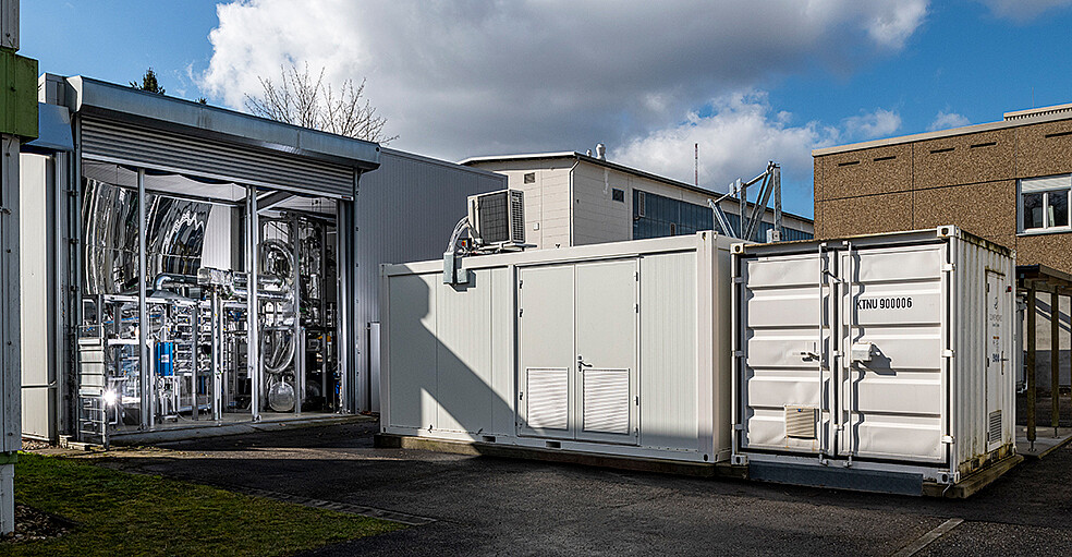 View of the entire NECOC pilot plant at Campus North of KIT: direct air capture (small container on the right), methanation (large container in the center), methane pyrolysis (set-up in the hall on the left). The new process for the utilization of the greenhouse gas carbon dioxide in the form of the end product carbon black is tested in the integrated experimental plant. (Image: KIT)