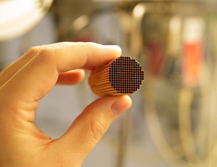 Hand hält ein zylindrisches Katalysatorbauteil mit vielen kleinen, gleichmäßig angeordneten Kanälen. Die Innenflächen dienen als Träger für Nanopartikel, die Schadstoffe im Abgas katalytisch zersetzen. Im Projekt PoWer entstehen darauf aufbauend neue Katalysatoren für Wasserstoff-Verbrennungsmotoren. (Bild: F. Maurer / KIT ITCP)
