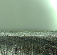 Microscopy of the bond: This sectional view shows a thin layer of bonding material and fine granules at the top and the metallic component to be connected at the bottom.