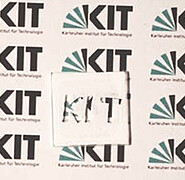 The brilliant white optic is demonstrated: Microstructured polymer coating on a glass plate with KIT logo as negative. (Image: Institute of Microstructure Technology / KIT)