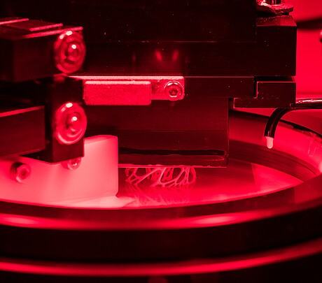 Blick ins Innere der Anlage: In einer mit Schlicker gefüllten Wanne wird ein Bauteil lithografisch gedruckt. Initiiert durch UV-Licht härtet eine komplexe Struktur mit glatten Oberflächen aus. Erst durch die fortschrittliche Fertigungstechnik können Multimaterialbauteile gedruckt werden. (Bild: KIT)