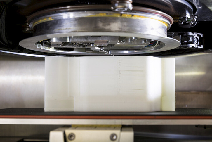 Based on the ARBURG freeformer, an additive production of fibre-reinforced plastic elements has been put into practice. The method incorporates a yarn infeed that rotates around the plastic discharge nozzle. The plasticised plastic is discharged onto the fibre, which is positioned below the discharge nozzle, and thus implements it directly into the element. (Image: Patrick Langer / KIT)