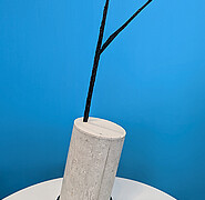 A piece of black reinforcement made of carbon fiber-reinforced plastic protrudes from a concrete cylinder used as a demonstrator. The free end of the reinforcement is bent into a loop. (Image: KIT)