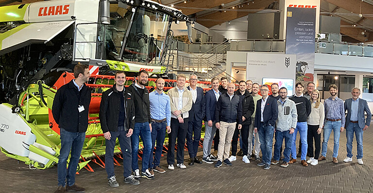 Eine Gruppe von Projektbeteiligten steht in einer Ausstellungshalle vor einer großen Landmaschine des Herstellers CLAAS. Das Foto wurde bei einem Konsortialtreffen des PoWer Projekts aufgenommen, bei dem Entwicklungen rund um Wasserstoff Antriebssysteme und neue Komponenten für Nutzfahrzeuge diskutiert wurden.