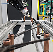 In der Karlsruher Forschungsfabrik am KIT: Die Roboterzelle für die Herstellung von Bewehrungen sieht aus wie ein futuristischer Webstuhl mit Metallrahmen und Kupferspulen, zwischen die schwarze Gummibänder gespannt sind. (Bild: KIT)