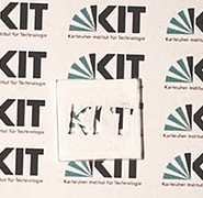 Mikrostrukturierte Polymerbeschichtung auf einer Glasplatte mit KIT-Logo als Negativ. (Bild: Institut für Mikrostrukturtechnik / KIT)