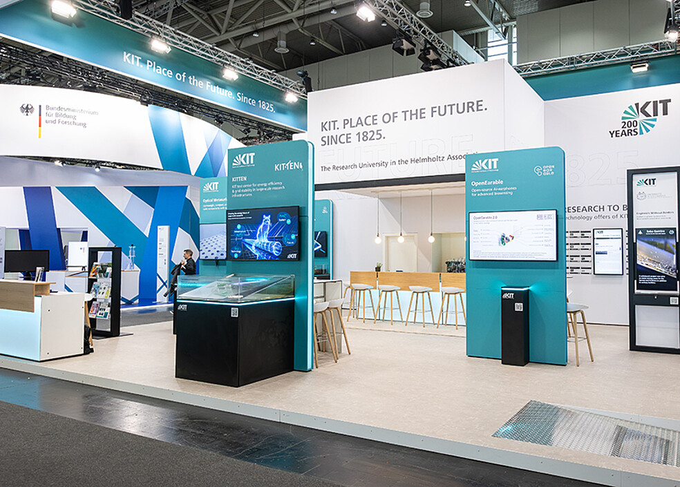 Große Gesamtansicht des KIT Messestands mit Informationssäulen, Präsentationsflächen, Sitzbereich und typischer Messebeleuchtung. Das KIT nutzt diese Plattform, um neue Technologien aus seinen Forschungsinstituten sichtbar zu machen und mit Unternehmen über gemeinsame Innovationsprojekte ins Gespräch zu kommen. (Bild: KIT)